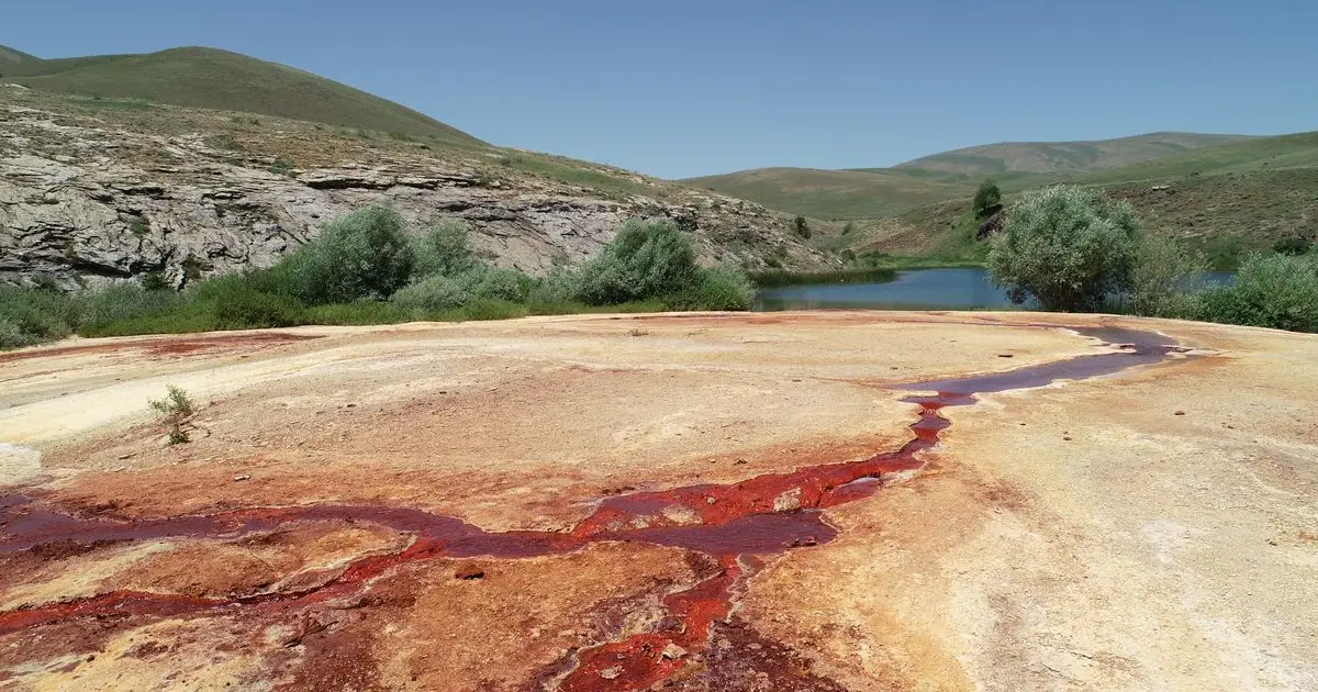 Lac cu apă roșiatică și drum săpat în stâncă, între pereți de 500 m